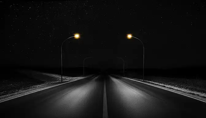 Long dark open road stretching into the distance at night sparsely lit by overhead lights.